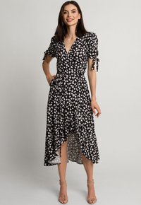 Czarna sukienka w kwiaty z krótkimi bufkami, akcentami do wiązania i asymetrycznym dołem. Lekka tkanina z małym białym wzorem kwiatowym.