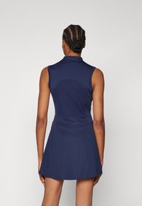 Mörkblå ärmlös polo-klänning med en åtsittande överdel och utsvängd kjol. Tillverkad av mjukt, texturerat tyg med en klassisk kragsdesign.