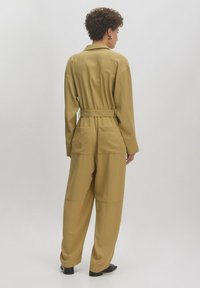 Khaki-Overall mit tailliertem Schnitt und weitem Bein, ausgestattet mit einem Kragen, zwei Gesäßtaschen und langen Ärmeln mit Knopfdetails.