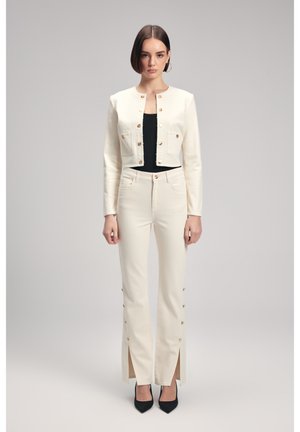 Veste crème coupée avec des boutons dorés et deux poches avant, assortie à un pantalon large crème avec des fentes latérales et des accents de boutons dorés.