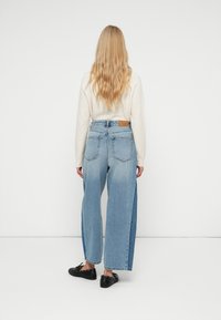 Helle blaue Denim-Hosen imweit geschnittenen Stil mit zweifarbigen Seiten, fünf Taschen und einem braunen Lederpatch am hinteren Bund.