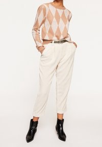 Persikofärgad och vit diamantmönstrad stickad tröja, krämfärgade kordflöjlsbyxor med upprullade benslut, och svarta ankelstövlar med spetsiga tår och spänne.