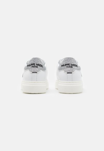 Zapatillas blancas con una parte superior de cuero suave, cuentan con un talón plateado brillante y la marca "Philippe Model Paris" en negro en la parte trasera.