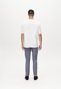 Camicetta bianca a maniche corte con orlo diritto, abbinata a pantaloni grigi chiari. L'outfit è completato da scarpe nere e un cappellino nero.