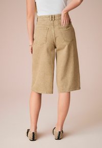 Culotte in denim beige con vita alta, due tasche posteriori e cuciture a contrasto, abbinate a calzature a trama aperta.