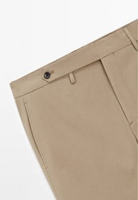 Pantaloni beige con taglio classico, dotati di chiusura a bottone, tasche laterali e texture del tessuto liscia.