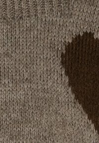 Stickad textil med en ljusbrun botten och ett mörkbrunt hjärtmönster. Texturen är ribbad och mysig, vilket framhäver dess mjukhet.