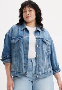 Ανοιχτό μπλε τζην μπουφάν με χαλαρή εφαρμογή, διαθέτει μεγάλες μπροστινές τσέπες, κλείσιμο με κουμπί και αναδιπλωμένα μανίκια. Φοριέται πάνω από λευκό πουκάμισο.