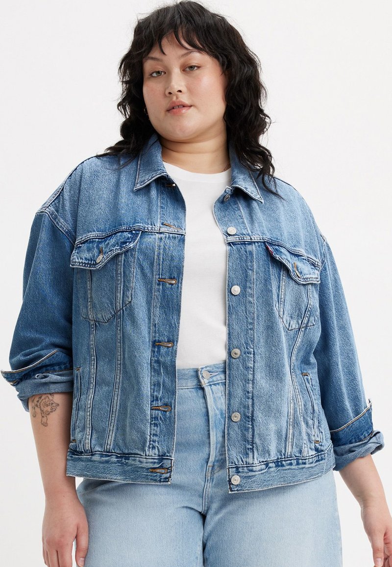 Ανοιχτό μπλε τζην μπουφάν με χαλαρή εφαρμογή, διαθέτει μεγάλες μπροστινές τσέπες, κλείσιμο με κουμπί και αναδιπλωμένα μανίκια. Φοριέται πάνω από λευκό πουκάμισο.