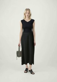 Top negru ajustat, asortat cu o fustă neagră fluidă, purtat cu pantofi cu vârf deschis negri. O geantă mică cu textură adaugă detaliu ținutei.