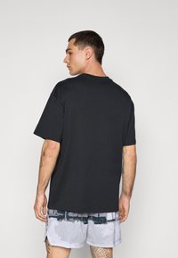 Sort bomulds T-shirt med korte ærmer, rund hals og en afslappet pasform, båret med mønstrede grå sportshorts.