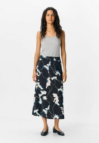 Jupe longue noire avec des motifs floraux abstraits bleus et blancs, présentant une texture lisse et une silhouette fluide. Portée avec un débardeur gris.