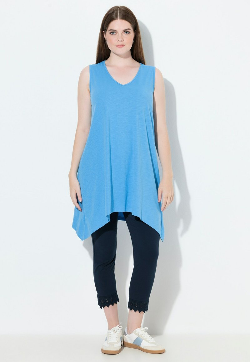 Túnica azul sin mangas con escote en V, de corte suelto y dobladillo curvado. Combinada con leggings marinos con borde de encaje y zapatillas blancas.