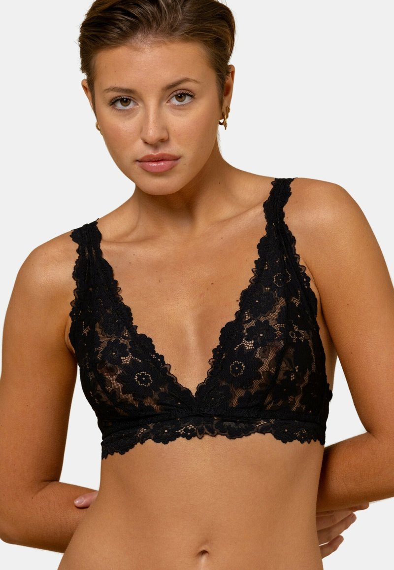 Soutien-gorge en dentelle noire avec un décolleté en V profond, un motif floral et des bords festonnés. Des fines bretelles ajustables complètent l'aspect délicat.