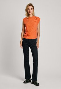 Oranje, kort-ärmige top met een gedrapeerd ontwerp; gecombineerd met strakke zwarte jeans en zwarte chunky-soled laarzen. Eenvoudige, schone lijnen.