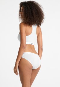 Witte katoen sportbeha met een racerback ontwerp en zwarte logo band, gecombineerd met bijpassende witte slip met vergelijkbare logo detail.