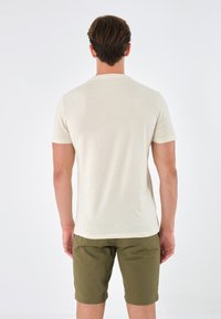 Kortermet beige t-skjorte med rund hals, kombinert med olivengrønne shorts. Stoffet ser mykt og lett ut.