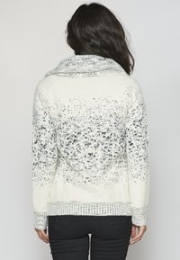 Vit och grå mönstrad tröja med cowl-hals, stickad textur och ribbad nederkant, med en övertoning som går från grå till vit.