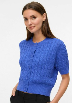 Korte mouwen blauwe cardigan met een gestructureerd kabelbinding ontwerp, geribbelde kraag en knoopsluitingen. Draagt een zwarte broek.