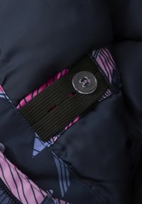 Marinblått puffer tyg med ett rosa och grått geometriskt mönster, med en elastisk rem som är fäst med en metallknapp.