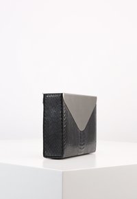 Taška s černým hadím potiskem má šedou trojúhelníkovou klopu, obdélníkový tvar, hladký povrch a jemný lesk; vyniká minimalistickým designem.