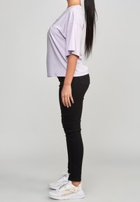 Ljuslila oversized T-shirt med korta ärmar, ihopparad med svarta slim-fit jeans och vita sneakers med guldaccenter.