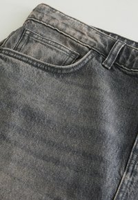 Zbliżenie wyblakłych czarnych dżinsów z denimu, ukazujące przednią kieszeń, kieszonkę na monety, pętlę na pasek oraz szczegóły szwów na talii.