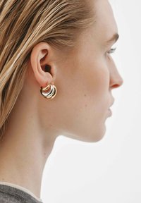 Pendientes de aro en capas de oro y plata con una superficie suave y reflectante, exhibidos en un modelo con cabello lacio.