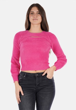 Maglione corto fuzzy rosa con scollatura rotonda e maniche lunghe, caratterizzato da un'apertura a chiave sul davanti. Abbinato a jeans neri.