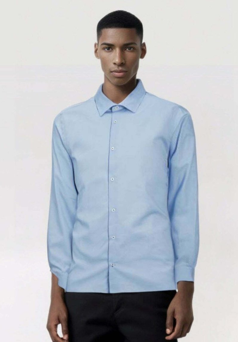 Camisa de manga larga azul claro con cuello puntiagudo, botones frontales y una textura suave. Combinada con pantalones oscuros. Diseño simple y moderno.