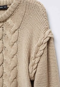 Beiger Strickpullover mit einem strukturierten Zopfstrickmuster auf der Vorderseite und geflochtenen Akzenten an den Ärmeln. Grob gestricktes Garn und gerippter Rundhalsausschnitt.