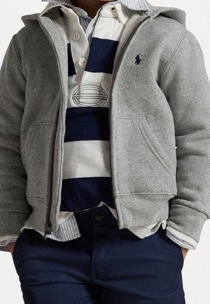 Grauer Zip-Hoodie über einem navy- und weißen gestreiften Polo, geschichtet mit einem hellblauen Vichykaro-Kragen, kombiniert mit navyfarbenen Hosen.