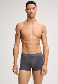 Harmaat bokserialushousut kuvioidulla vyötärönauhalla. Kangas on sileä, istuva ja joustava, suunniteltu mukavuutta ja liikkuvuutta varten.