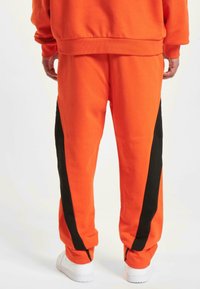 Orange sweatpants made of cotton blend, featuring black side stripes, tapered cuffs, and elastic waistband. Pair with white sneakers.
