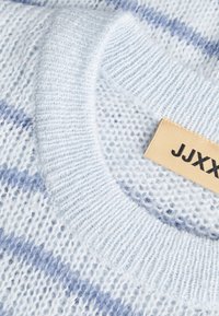 Világos kék kötött pulóver texturált anyagból, váltakozó világoskék és levendulaszínekkel. Bevonattal ellátott bézs címke, rajta "JJXXX" felirattal fekete színben.