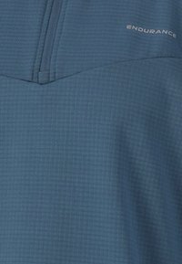 Modrý sportovní top s texturovaným, žebrovaným vzorem a designem na poloviční zip. Obsahuje decentní logo vytištěné bílou barvou na horní straně.