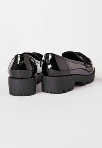 Czarne buty z lakierowanej skóry z masywną czarną gumową podeszwą. Widok od tyłu ukazuje gładkie, błyszczące wykończenie oraz ozdobną kokardę.