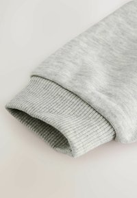 Harmaa hupparivarvas, jossa on ribbikuviointi, pehmeä kangas ja rento muoto. Esitetty taitettuna reunasta varmuuden vuoksi.