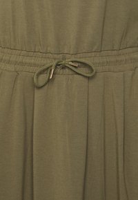 Olivgrüner Stoff mit gerafftem Taillenbund, ausgestattet mit einem Kordelzug mit goldenen Akzenten. Weiche Textur und fließendes Design.