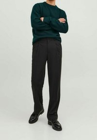 Mörkgrön stickad tröja med rund hals, i kombination med svarta plisserade byxor och svarta läderskor, vilket skapar en klassisk och strömlinjeformad outfit.