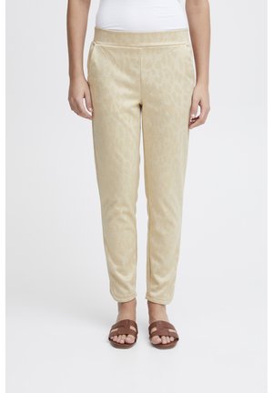 Beige jogger pants with a textured leopard pattern, elastic waistband, side pockets, and a tapered leg design, paired with brown sandals.