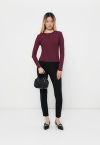 Top lungo a maniche rigate bordeaux, design aderente. Pantaloni neri slim, abbinati a una borsa nera texturizzata e scarpe nere a punta.