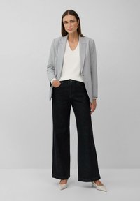 Lichtgrijze op maat gemaakte blazer, witte v-hals trui en hoogsluitende zwarte wijde broek, aangevuld met beige puntenhakschoenen.