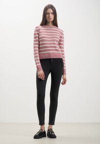 Maglione a righe rosa e bianche con scollatura rotonda, bordo a coste e maniche lunghe, abbinato a jeans skinny neri e mocassini neri lucidi.