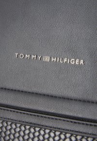 Borsa a mano in pelle nera con texture, caratterizzata dal logo "TOMMY HILFIGER" in argento. Il design include un'accenno intrecciato e un pannello liscio.