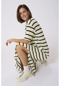 Gebreide jurk met gele en zwarte strepen, korte mouwen, hoge zijsplitten. Gecombineerd met witte enkelsokken en crème sneakers.