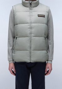 Gilet imbottito verde chiaro, con colletto alto, zip frontale e tasche laterali. Indossato sopra una maglia grigia a maniche lunghe.