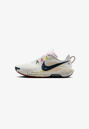 Chaussure de trail Nike blanche avec œillets multicolores, swoosh noir, semelle intermédiaire mouchetée et languette à l’arrière sur fond blanc.