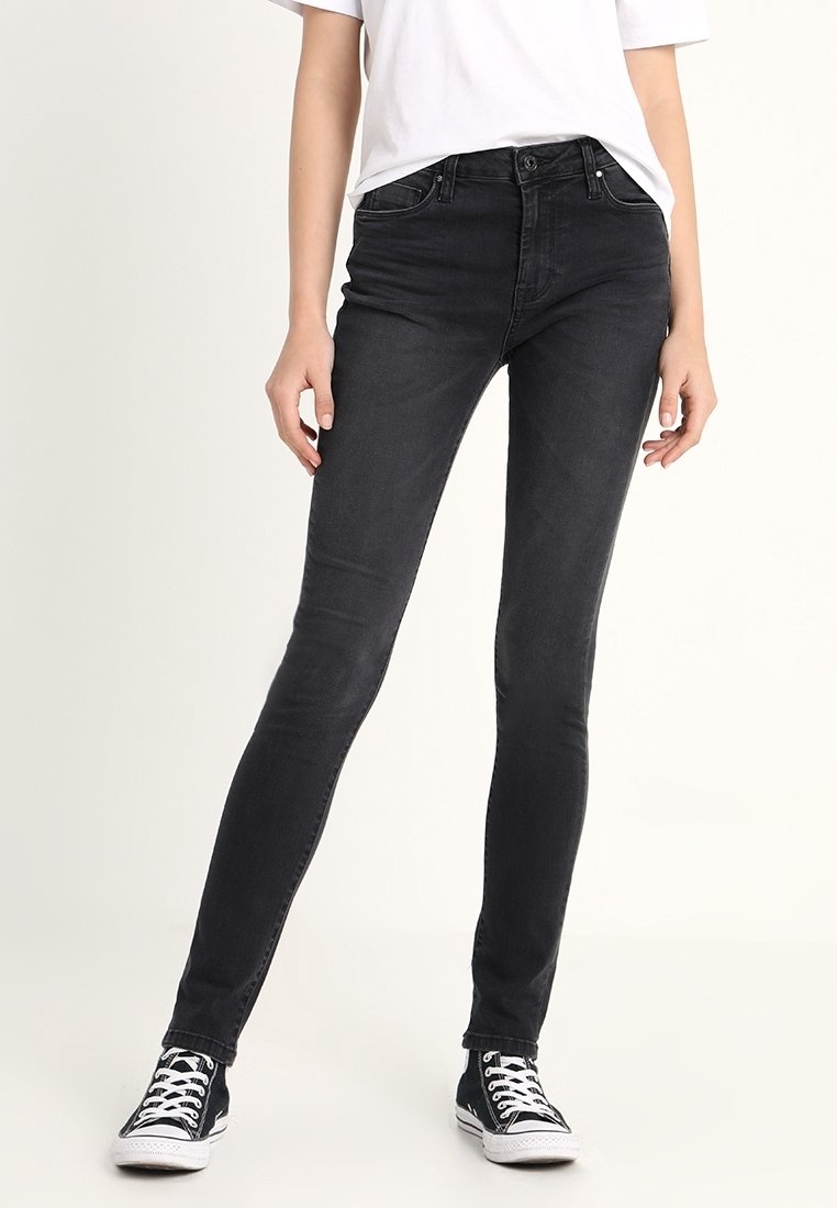 Jeans skinny negros de denim, con un diseño ajustado, cintura de altura media y detalles de costura sutiles, combinados con zapatillas negras.