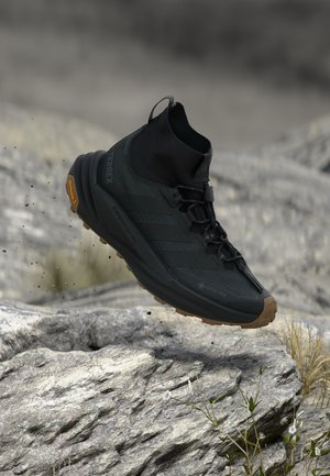 Sort high-top vandresko med robust sål, Gore-Tex vandtæthed og snørebånd, svævende over klippefyldt terræn.